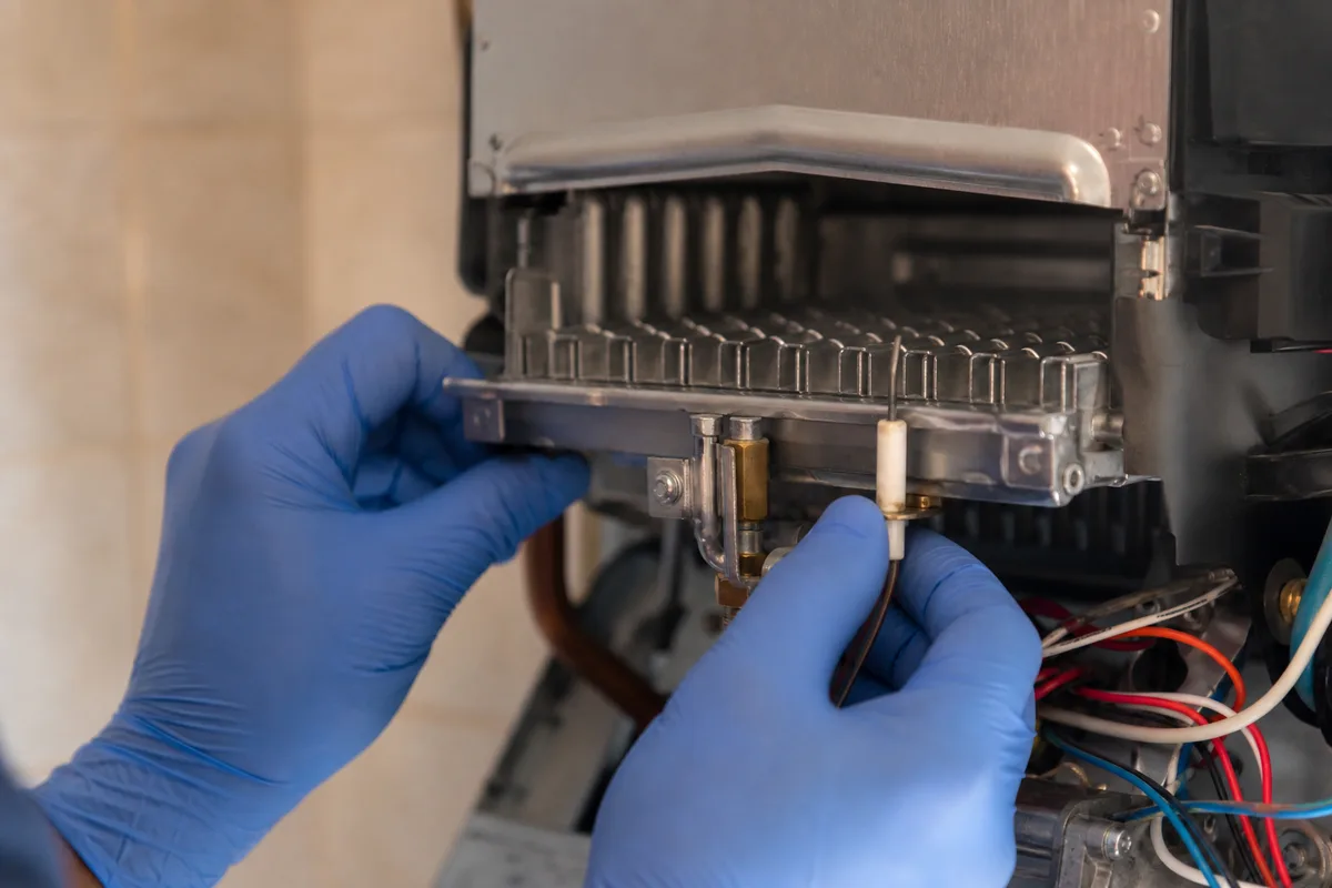Chaudière gaz murale ouverte dans une cuisine marseillaise, mains gantées d&rsquo;un technicien contrôlant le brûleur