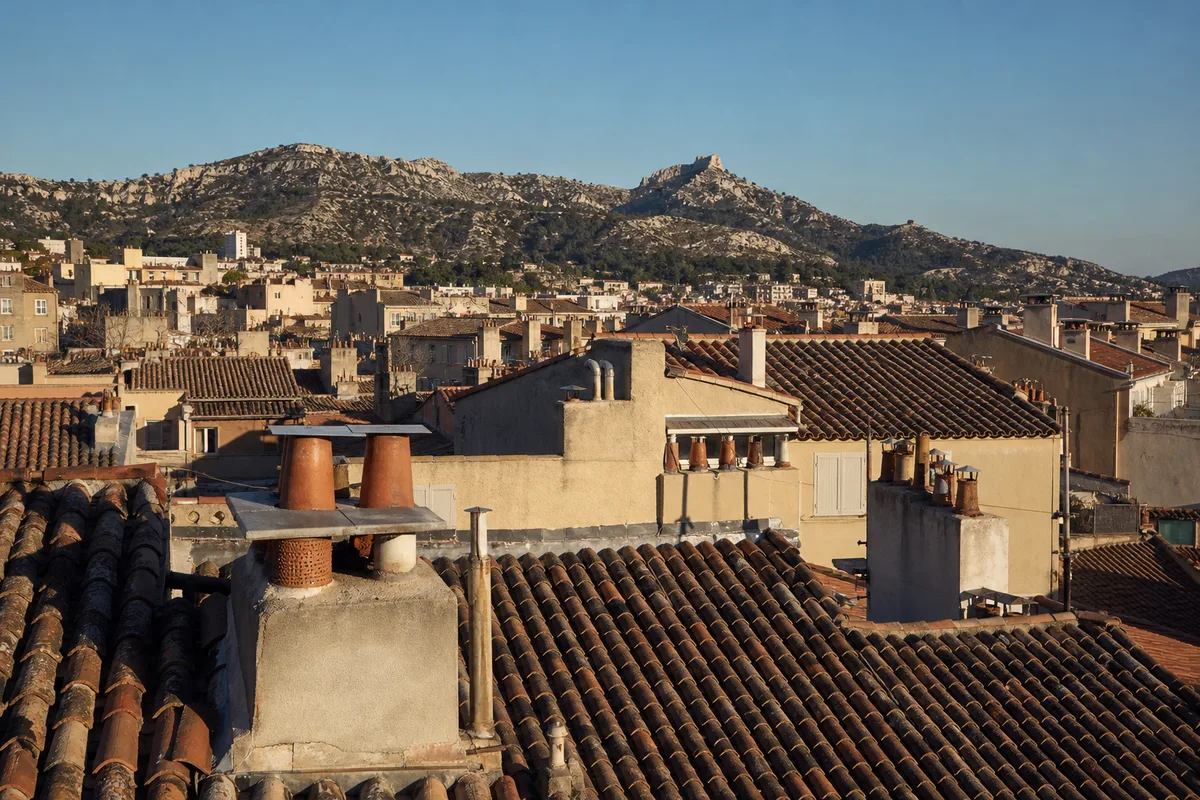 Toits de tuiles romanes et souches de cheminée d&rsquo;un quartier marseillais sous une lumière méditerranéenne de fin d&rsquo;après-midi