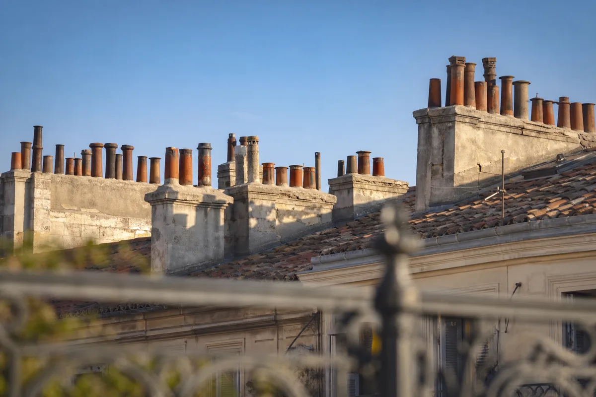 Souches de cheminée maçonnées alignées sur les toits d&rsquo;un immeuble ancien du centre de Marseille